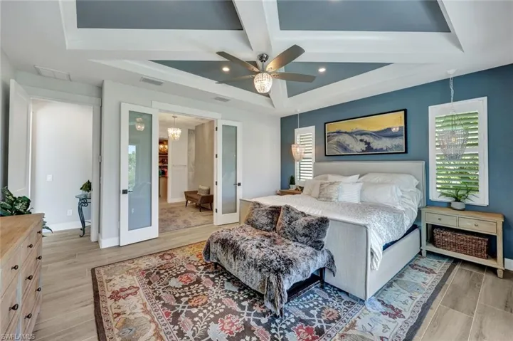 Bedroom with light wood-type flooring, ceiling fan, a chandelier, coffered ceiling, and beam ceiling