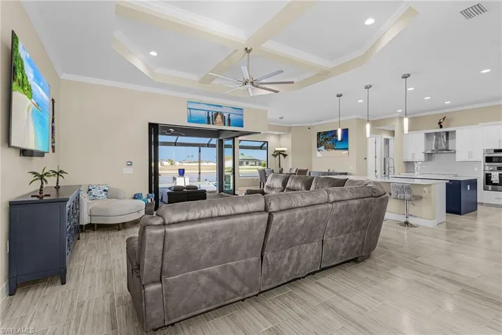 Living room featuring coffered ceiling, beamed ceiling, ornamental molding, and ceiling fan