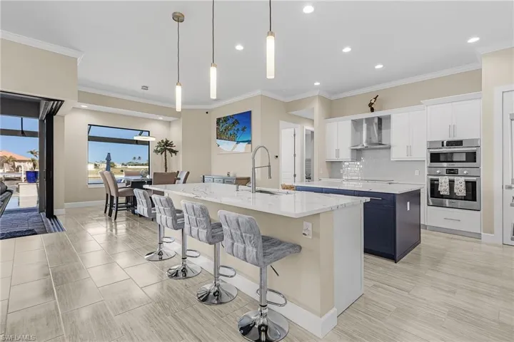 Kitchen with white cabinets, sink, a kitchen island with sink, and wall chimney range hood