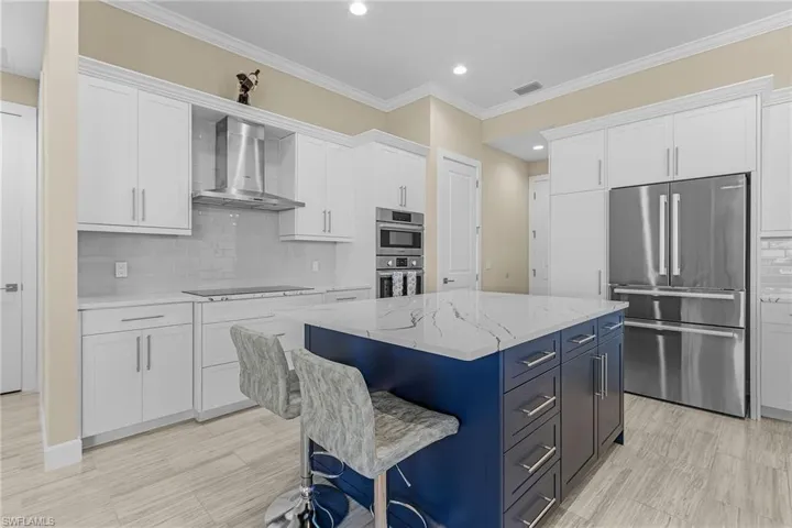 Kitchen featuring white cabinetry, stainless steel appliances, and wall chimney range hood