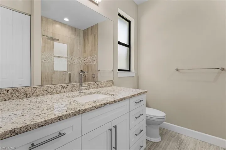 Bathroom with hardwood / wood-style flooring, vanity, toilet, and a tile shower
