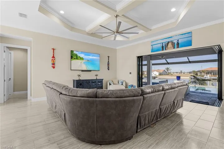 Living room featuring ornamental molding, coffered ceiling, and ceiling fan