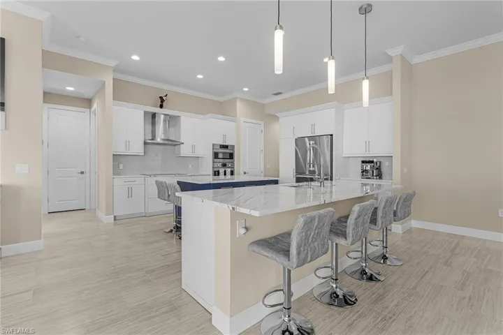 Kitchen with white cabinets, a large island with sink, sink, and wall chimney exhaust hood