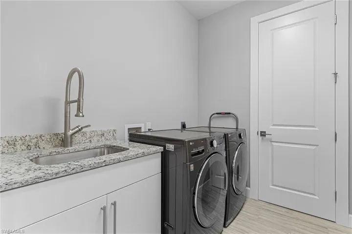 Laundry area featuring sink, light hardwood / wood-style flooring, cabinets, and washing machine and clothes dryer