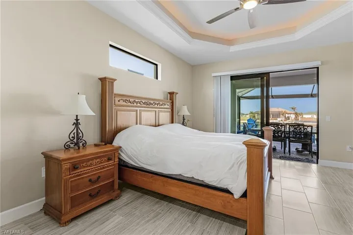 Bedroom featuring ceiling fan, a tray ceiling, multiple windows, and access to outside