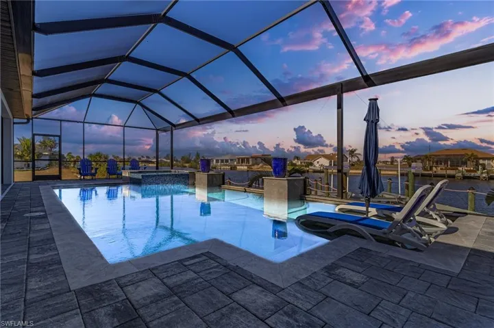 Pool at dusk with an in ground hot tub, glass enclosure, and a patio area