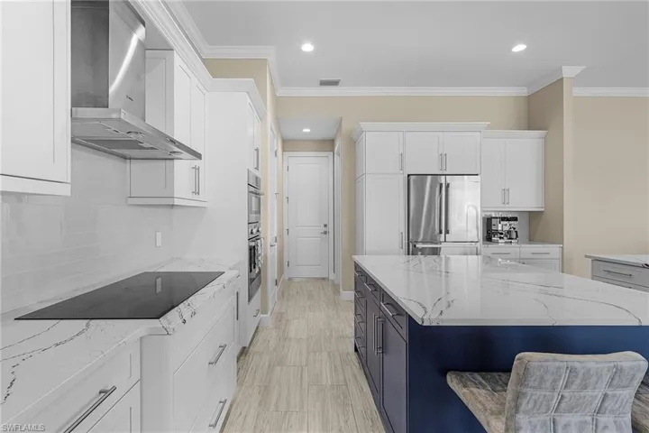 Kitchen featuring white cabinetry, wall chimney range hood, light stone counters, and appliances with stainless steel finishes