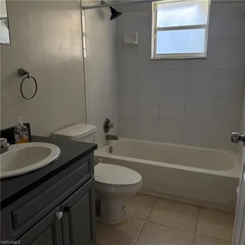 Bathroom featuring a white bathtub, tiled shower surround, and a dark grey vanity with an integrated sink