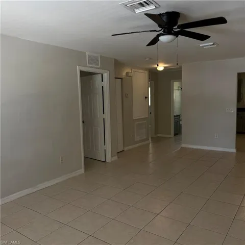 Spacious room featuring tile flooring, neutral wall tones, a ceiling fan with integrated lighting, and white trim molding