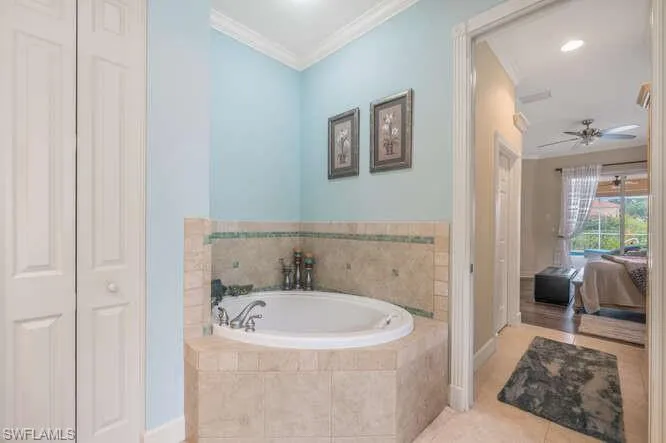 Bathroom with crown molding, tile patterned flooring, tiled tub, and ceiling fan