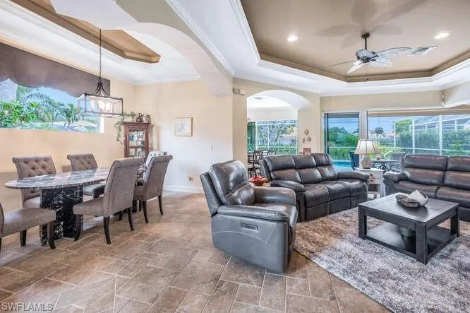 Living room featuring ceiling fan with notable chandelier, a tray ceiling, and crown molding