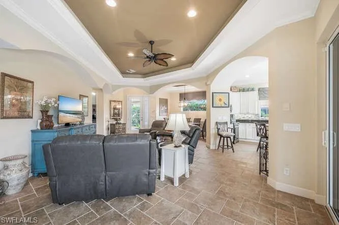 Living room featuring ceiling fan, a wealth of natural light, a tray ceiling, and crown molding