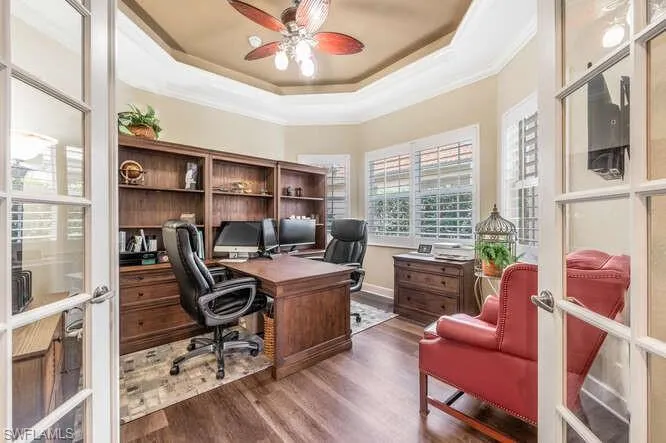 Home office featuring dark hardwood / wood-style flooring, french doors, ornamental molding, ceiling fan, and a tray ceiling