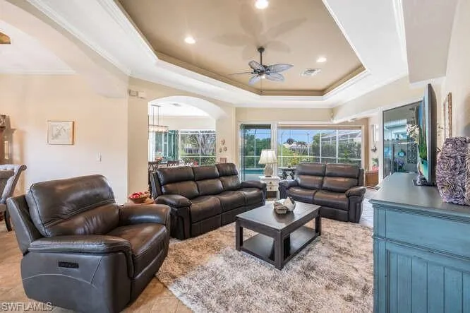 Living room with ceiling fan, light tile patterned floors, a tray ceiling, and ornamental molding