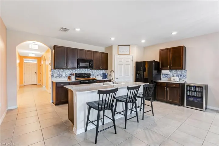 Kitchen featuring black appliances, light tile patterned flooring, decorative backsplash, arched walkways, and a kitchen bar