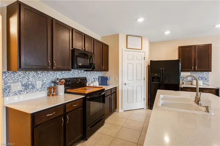 Kitchen with black appliances, dark brown cabinetry, tasteful backsplash, light tile patterned floors, and recessed lighting