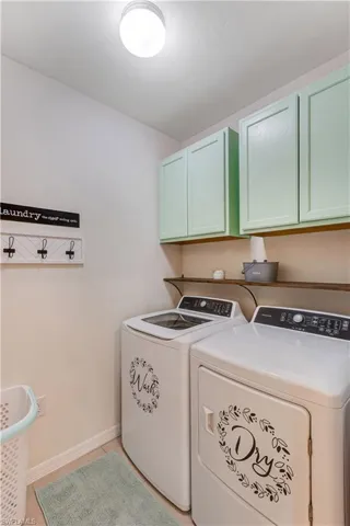 Washroom featuring cabinet space, washing machine and dryer, and light tile patterned floors
