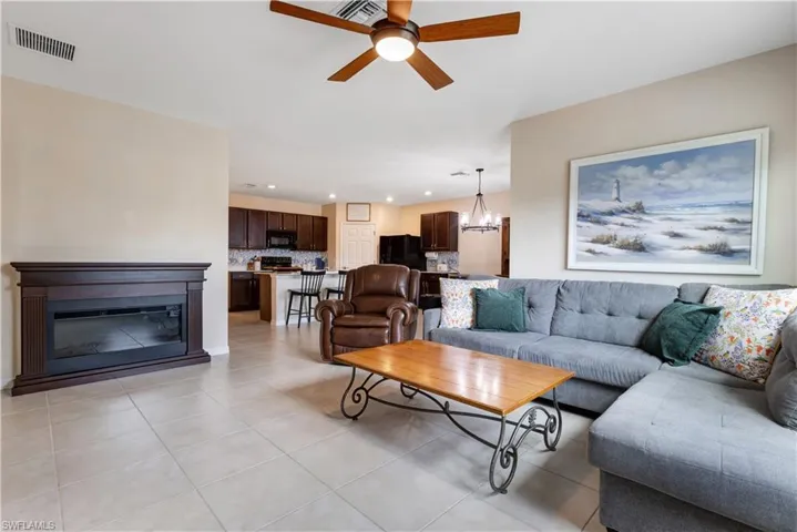 Living room with a ceiling fan, recessed lighting, light tile patterned floors, a chandelier, and a glass covered fireplace
