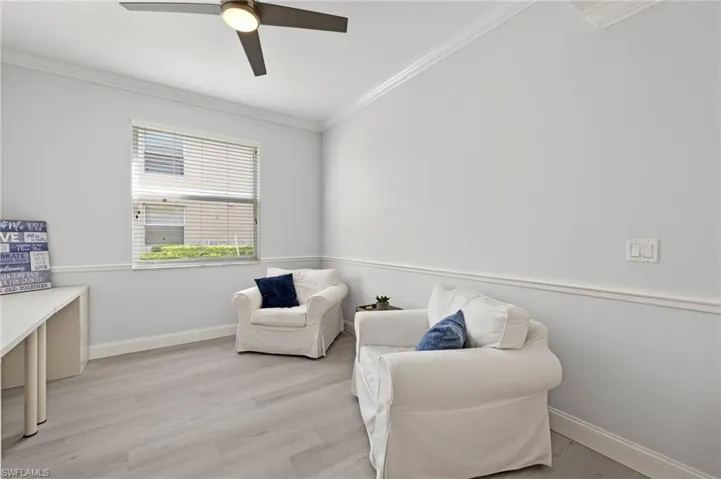 Living area with crown molding, baseboards, light wood-type flooring, and ceiling fan