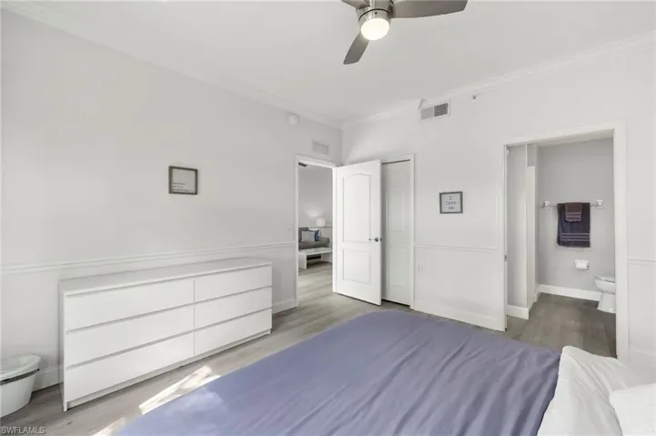 Unfurnished bedroom featuring ensuite bath, visible vents, ornamental molding, and wood finished floors