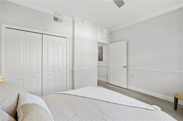 Bedroom with visible vents, baseboards, a closet, ornamental molding, and wood finished floors