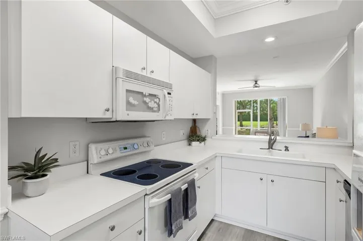 Kitchen with white cabinets, a sink, ornamental molding, light countertops, and white appliances