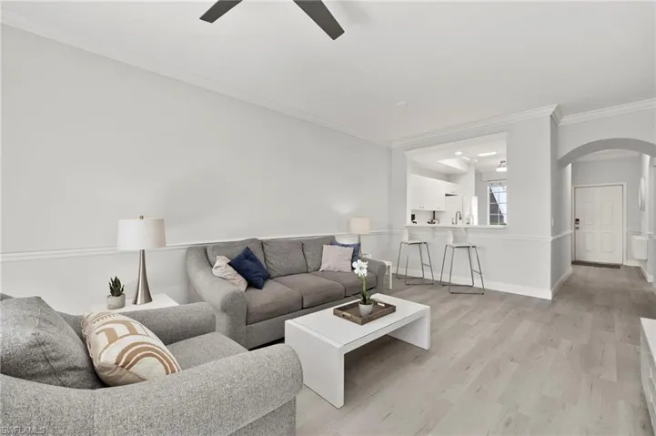 Living area featuring arched walkways, light wood-type flooring, ornamental molding, a ceiling fan, and baseboards