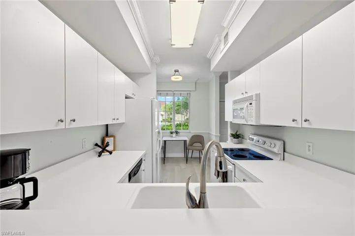 Kitchen featuring white appliances, white cabinetry, light countertops, crown molding, and a sink