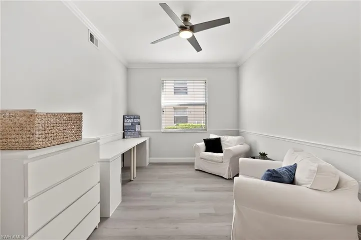 Living area featuring light wood-style floors, visible vents, ornamental molding, and ceiling fan