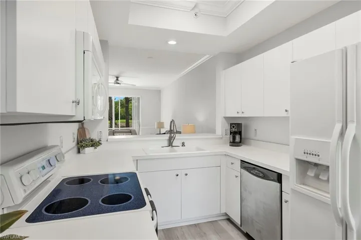 Kitchen with white appliances, white cabinetry, crown molding, ceiling fan, and a sink