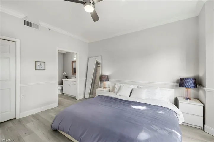 Bedroom featuring baseboards, ensuite bathroom, crown molding, light wood-style floors, and visible vents