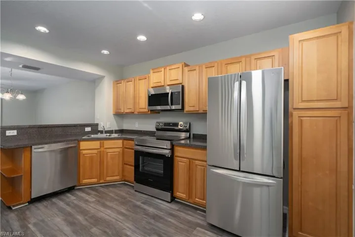 Kitchen featuring kitchen peninsula, stainless steel appliances, sink, an inviting chandelier, and dark hardwood / wood-style floors