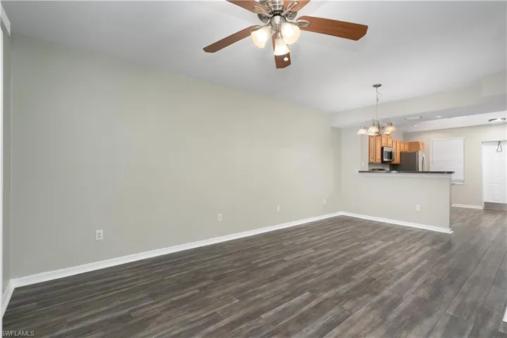 Unfurnished living room featuring ceiling fan with notable chandelier and dark hardwood / wood-style flooring