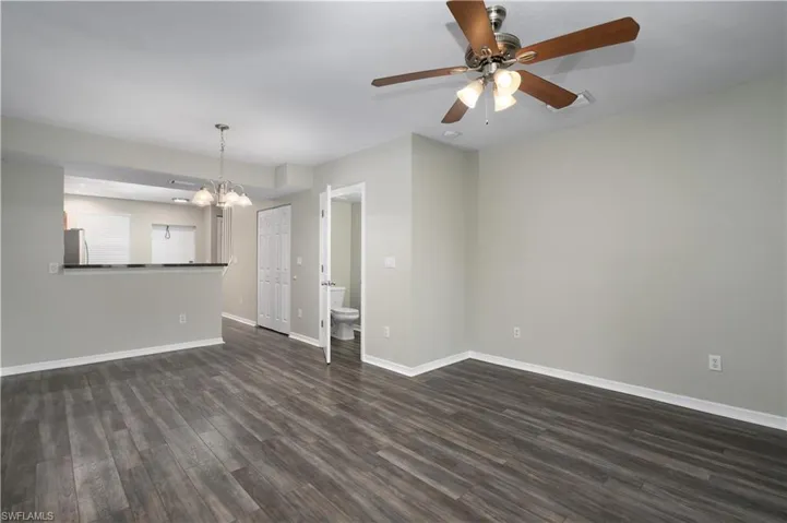 Unfurnished living room with dark wood-type flooring and ceiling fan with notable chandelier