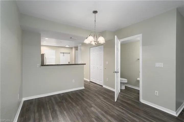 Empty room with dark hardwood / wood-style floors and a notable chandelier