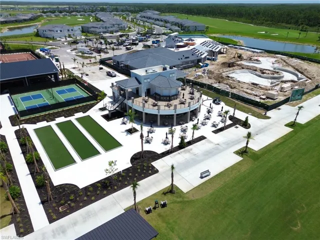 Community amenity center featuring a multi-story clubhouse, two pickleball courts, three bocce ball courts, and a paved outdoor lounge area