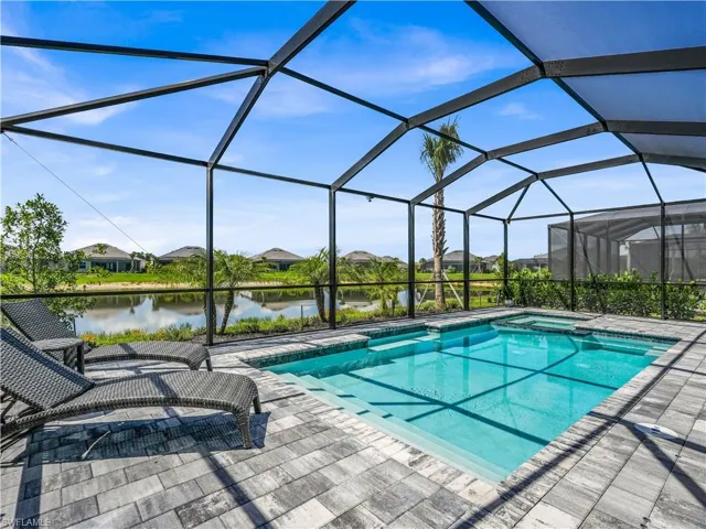 Screened pool enclosure featuring a rectangular swimming pool, integrated spa, paver decking, and a water-facing orientation