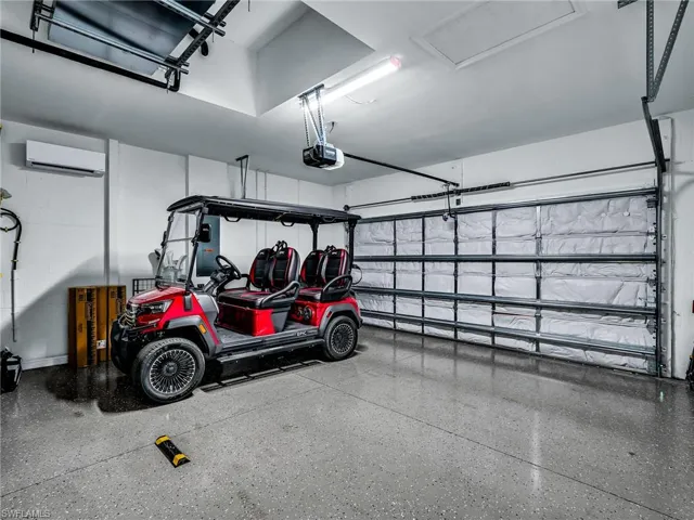 Spacious garage featuring an insulated door, polished concrete flooring, overhead lighting, and a wall-mounted mini-split system