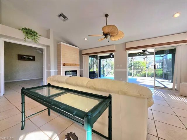 Living room with light tile patterned floors, a glass covered fireplace, a ceiling fan, a sunroom, and high vaulted ceiling
