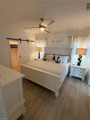Bedroom with a barn door for closet, light wood-style flooring, and a ceiling fan