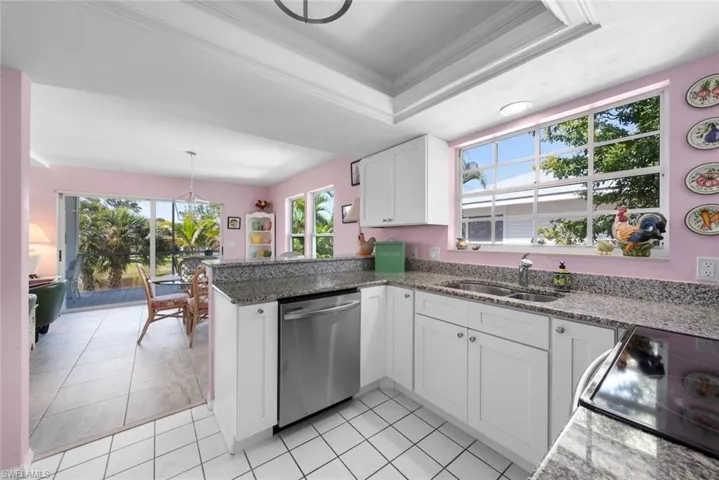 Kitchen featuring stainless steel dishwasher, a peninsula, white cabinetry, a sink, and a raised ceiling
