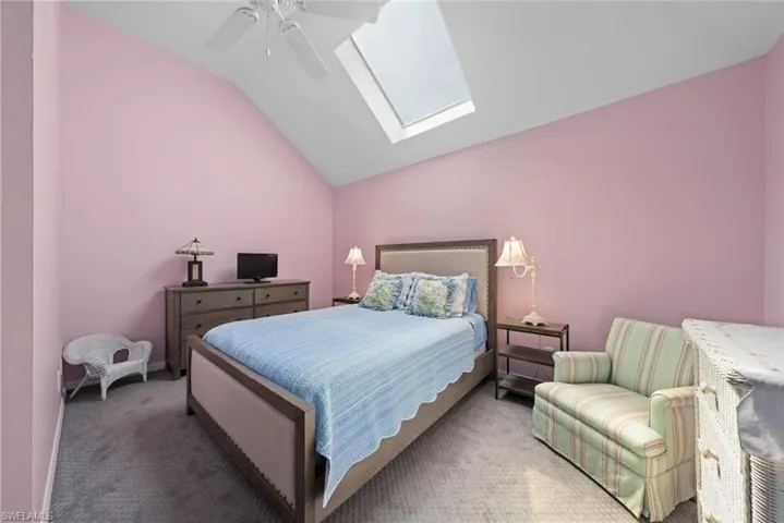 Bedroom featuring vaulted ceiling with skylight, baseboards, a ceiling fan, and carpet flooring