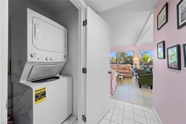 Laundry area with baseboards, laundry area, light tile patterned flooring, and stacked washer and clothes dryer
