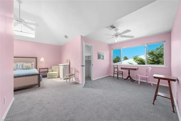 Carpeted bedroom featuring visible vents, baseboards, a ceiling fan, and lofted ceiling with skylight