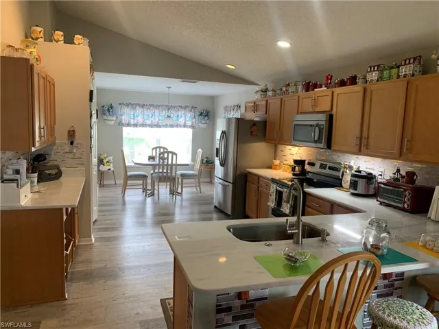 Kitchen with light hardwood / wood-style floors, appliances with stainless steel finishes, lofted ceiling, and decorative backsplash