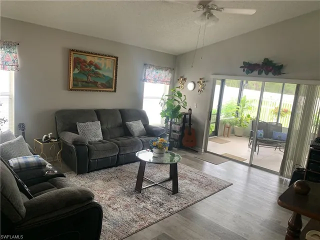 Living room with light wood-type flooring, ceiling fan, vaulted ceiling, and a textured ceiling