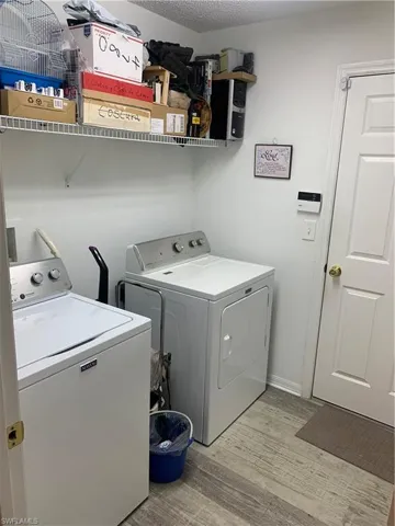 Laundry area featuring light wood-type flooring, washer and dryer, and a textured ceiling