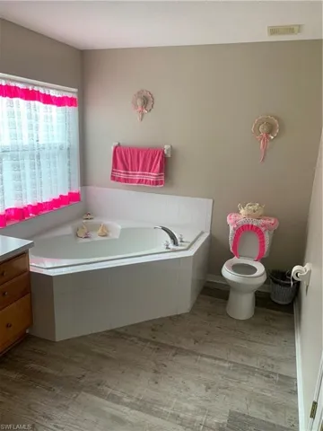 Bathroom featuring tiled tub, vanity, hardwood / wood-style flooring, and toilet