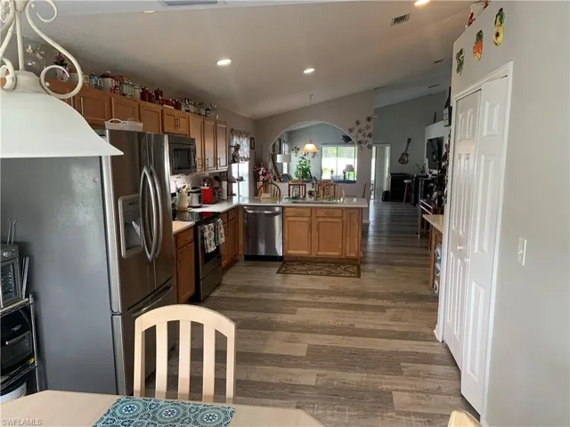 Kitchen with pendant lighting, vaulted ceiling, dark hardwood / wood-style floors, appliances with stainless steel finishes, and kitchen peninsula