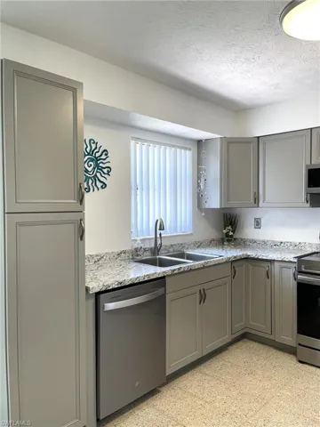 Kitchen featuring sink, light stone countertops, a textured ceiling, gray cabinetry, and stainless steel appliances